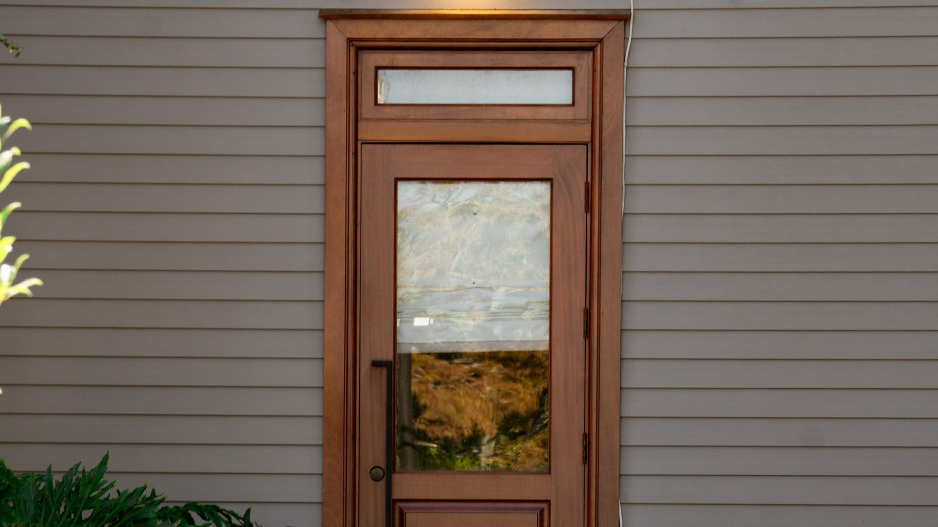 A wood storm door with a glass panel on a grey clapboard house